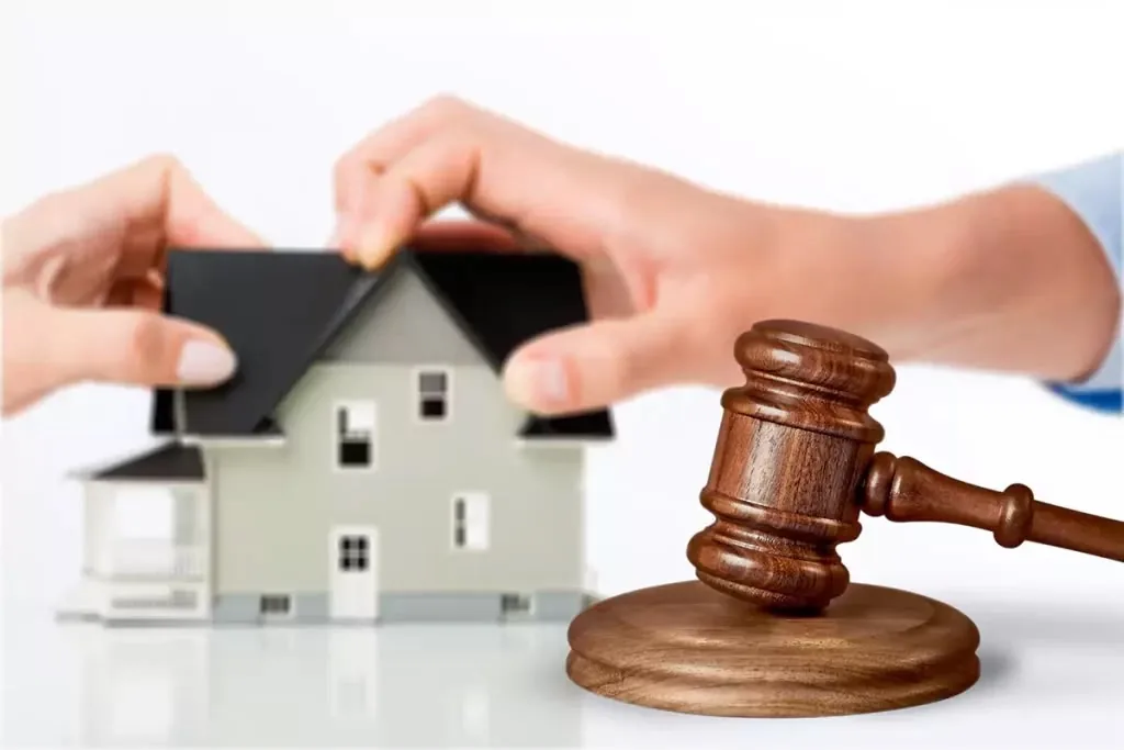 Two hands pulling at a model house beside a judge’s gavel
