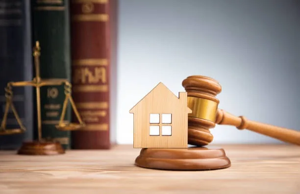A wooden house and a gavel in front of law books and the scales of justice